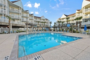 A swimming pool with lounge chairs, a covered area, and a multi-story building with balconies.