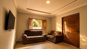 Um quarto com um sofá marrom, uma porta de madeira e uma janela com persianas.