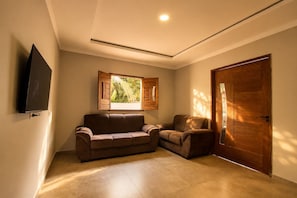 A room with a brown sofa, a wooden door, and a window with shutters. - Casa com Piscina Pertinho da Praia do Boqueir o (Japaratinga)