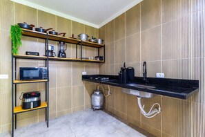 A kitchen with a black countertop, a built-in sink, a gas stove, a microwave, a coffee maker, and a gas cylinder. - Casa com Piscina Pertinho da Praia do Boqueir o (Japaratinga)