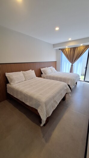 Une chambre d’hôtel moderne avec deux lits, une tête de lit en bois et une grande fenêtre avec des rideaux.