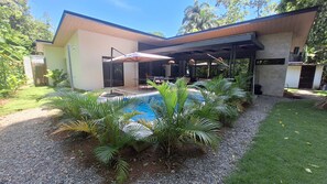 Ein modernes Haus mit Swimmingpool, überdachter Terrasse und üppiger Bepflanzung.