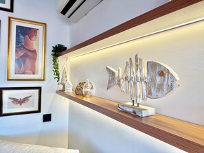 A modern interior with a wooden shelf displaying decorative items, a wall-mounted air conditioner, and framed artwork.