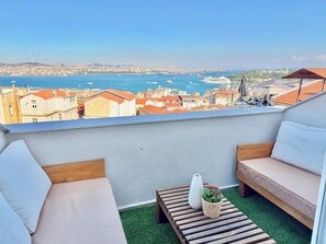 A balcony with a view of the sea, a sofa, a small table, and a potted plant.