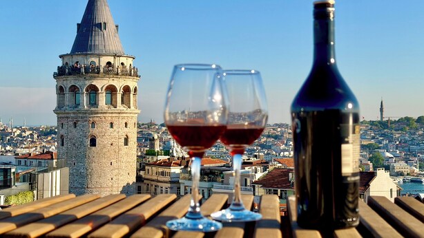 A view of a cityscape with a prominent tower and a table with two wine glasses and a bottle. - The Genoese Galata (İstanbul)