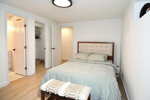 Ein Schlafzimmer mit einem Bett, einer Sitzbank, einem Kleiderschrank und einer Tür zu einem anderen Raum.
