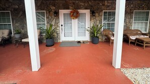 A covered porch with stone walls, a double door with a wreath, potted plants, wicker furniture, and ceiling fans.