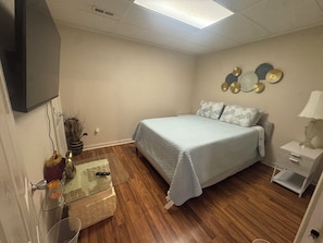 Ein Schlafzimmer mit einem Bett, einem Nachttisch, einer Lampe, dekorativen Wandelementen und einem Fernseher an der Wand.