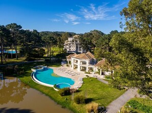Una casa grande con piscina, rodeada de césped cuidado y árboles.