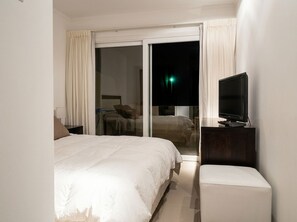 Habitación de hotel con cama, televisión, escritorio y puerta corrediza a un balcón.
