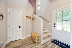 A staircase with a handrail, a white door, a wooden shelf, and a welcome mat.