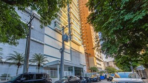 Un edificio a più piani con un parcheggio, veicoli e alberi.
