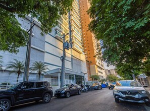Edifici de diverses plantes amb una plaça d'aparcament, vehicles i arbres.