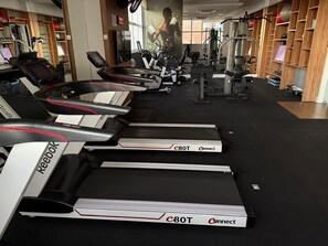 Ein Fitnessstudio mit Laufbändern, Krafttrainingsgeräten und einem großen Spiegel.