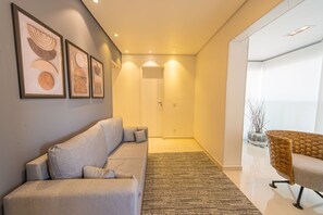 Ein modernes Wohnzimmer mit einer Couch, einem Korbstuhl und gerahmten Kunstwerken an der Wand.
