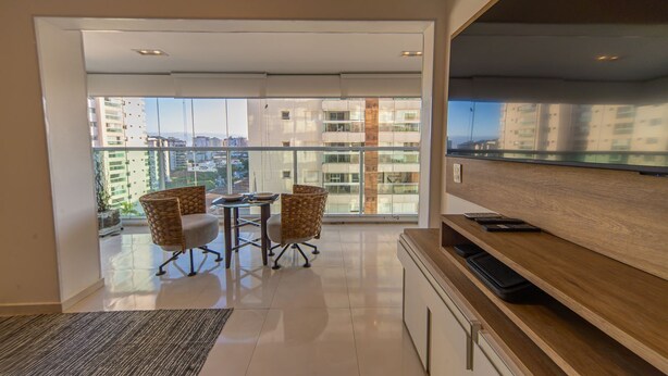 Un appartamento moderno con un balcone, un'area pranzo con sedie, una TV e vista sulla città.