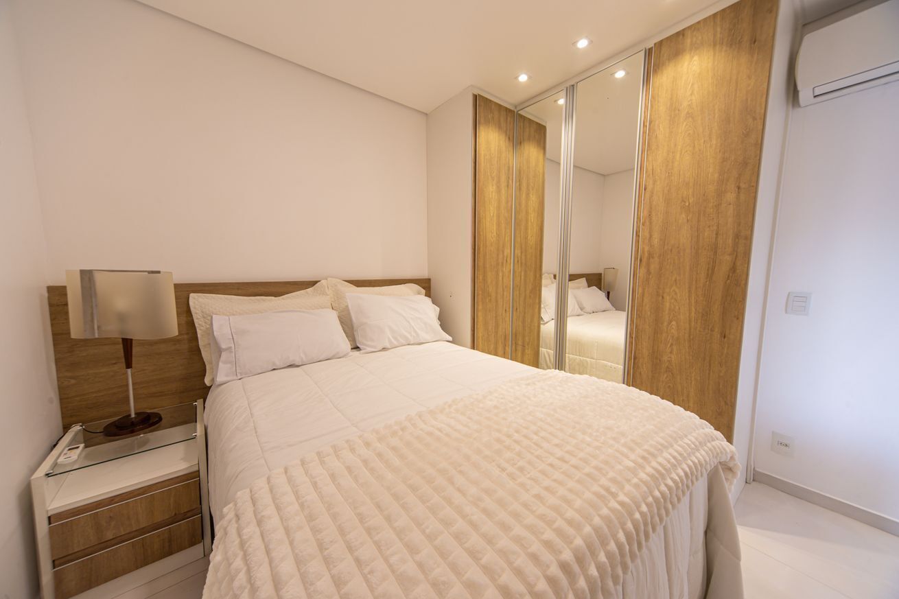 A bedroom with a bed, bedside table, lamp, wardrobe, and a mirror.