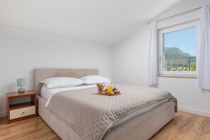 A bedroom with a bed, a nightstand, a tray of pastries, and a window with a mountain view. - Villa White Rose with heated pool in Kaštela (Kaštel Lukšić)