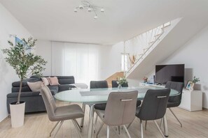 A modern living room with a glass dining table, grey sofas, and a staircase. - Villa White Rose with heated pool in Kaštela (Kaštel Lukšić)