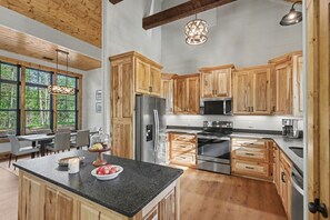 A modern kitchen with wooden cabinets, stainless steel appliances, and a large island with a bowl of fruit.