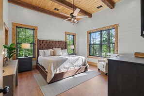 A bedroom with a large bed, wooden ceiling beams, and large windows.