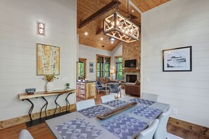 A spacious living area with a fireplace, a dining table with geometric-patterned placemats, and a large window overlooking greenery.