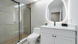 Un bany modern amb plat de dutxa de vidre, un vàter blanc i un lavabo amb mirall.