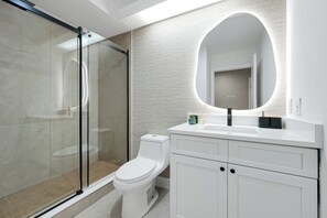 Ein modernes Badezimmer mit Duschkabine aus Glas, einer weißen Toilette und einem Waschtisch mit Spiegel.