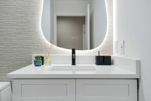 A modern bathroom with a white vanity, a round mirror, and a sink. - Studio near Epic Universe and Disney (Orlando)
