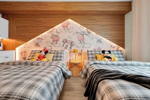 Ein Schlafzimmer mit zwei Betten, einer Holzbalkendecke und Wandtapete mit Mickey Mouse-Motiven.