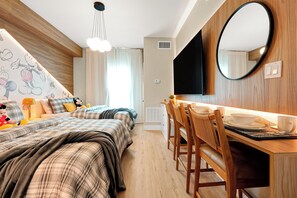 A modern bedroom with a bed, a desk with chairs, a flat-screen TV, and a large mirror. - Studio near Epic Universe and Disney (Orlando)