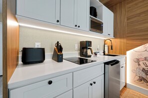 A modern kitchen with white cabinetry, a black coffee maker, and a built-in dishwasher. - Studio near Epic Universe and Disney (Orlando)
