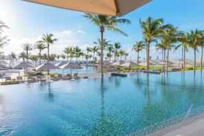 A pool area with lounge chairs and umbrellas, surrounded by palm trees. - 3BR Penthouse Loft, Rooftop Ocean View Terrace, Save 45% vs Garza Blanca Direct (Cancun)