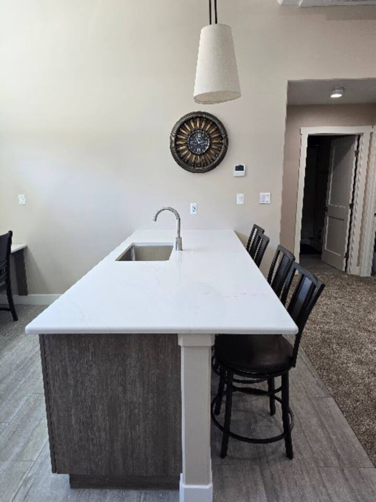 Una isla de cocina con un lavamanos, una lámpara colgante y un reloj de pared decorativo.