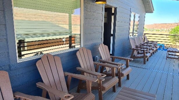 A covered outdoor seating area with Adirondack chairs and a table, a large window, and a door leading to the interior. - Moab Beauty Custom Home (Moab)