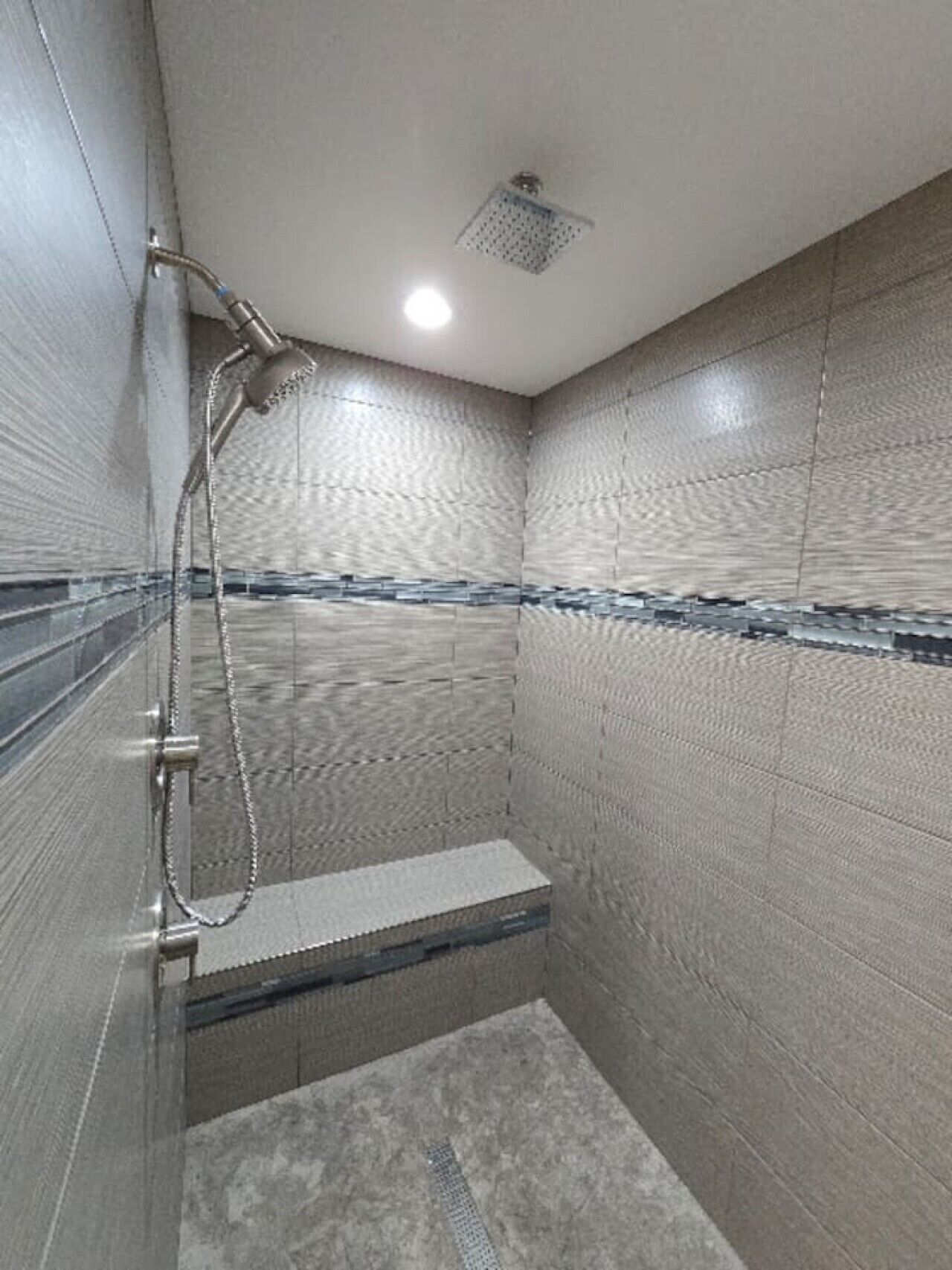 Un baño pequeño revestido con azulejos, con un cabezal de ducha de mano y un asiento integrado.