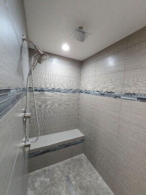 Ein kleines Duschbad mit Fliesen, einer Handbrause und einer fest installierten Sitzgelegenheit.
