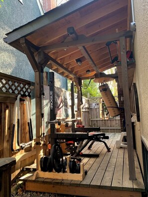 An outdoor gym setup with a bench press, dumbbells, and a punching bag. - Family Favourite in Kitsilano.  Outdoor Gym and large cedar deck. (Vancouver)