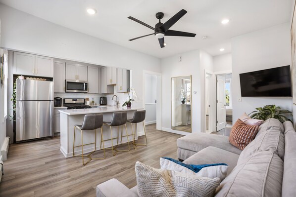 A modern kitchen with a central island, bar stools, and a ceiling fan.