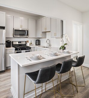 A modern kitchen with white cabinetry, stainless steel appliances, and a central island with bar stools.
