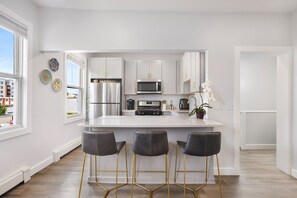 A modern kitchen with white cabinets, a stainless steel refrigerator, a microwave, and a large island with bar stools.