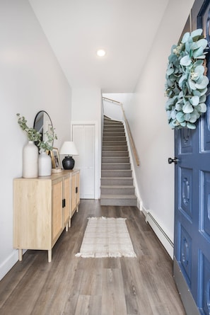 Ein Flur mit einem Holzschrank, einem Spiegel, einer Tür mit blauem Rahmen und einer Treppe, die in ein weiteres Zimmer führt.