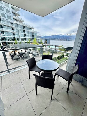 Ein Balkon mit rundem Tisch und Stühlen, Blick auf ein modernes Gebäude und ein Gewässer.