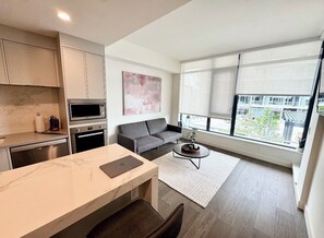 A modern kitchen with a marble countertop, a dining area with a table and chairs, a gray sofa, a coffee table, and large windows with blinds. - Waterfront luxurious 2-bedroom/2 bath apartment in fabulous Kelowna (Kelowna)
