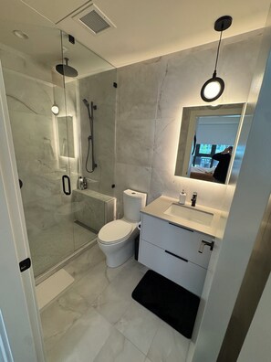 Ein modernes Badezimmer mit einer Glaskabine zur Dusche, Toilette, Waschbecken und Spiegel.