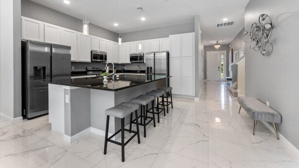 A modern kitchen with white cabinets, stainless steel appliances, a central island with bar stools, and a marble floor. - 12BR/11BA Home w/Private Pool Near Parks (MA36) (Kissimmee)