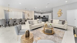 A modern living room with a dining area, a kitchen in the background, and a chandelier. - 12BR/11BA Home w/Private Pool Near Parks (MA36) (Kissimmee)
