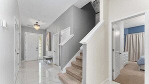 A hallway with a marble floor, a staircase, and a bedroom with a bed and curtains. - 12BR/11BA Home w/Private Pool Near Parks (MA36) (Kissimmee)