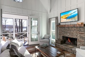 A living room with a fireplace, a television, and a view of a snowy landscape through large windows. - Elegant Murray Cove at Lake Burton (Tiger)