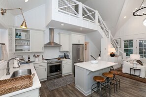 A modern kitchen with white cabinetry, stainless steel appliances, a central island with stools, and a staircase leading to an upper level. - Elegant Murray Cove at Lake Burton (Tiger)